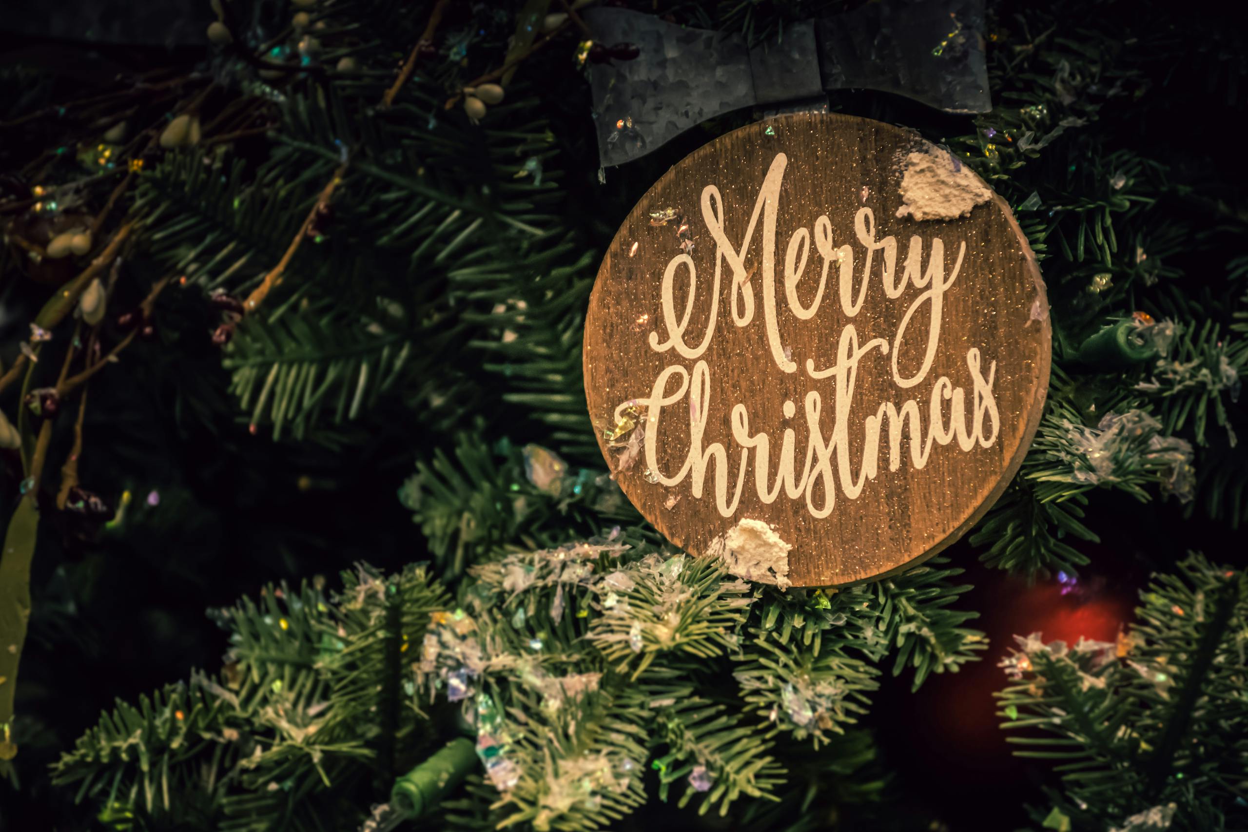 Close-up of a Merry Christmas ornament on a decorated fir tree, evoking festive holiday spirit.