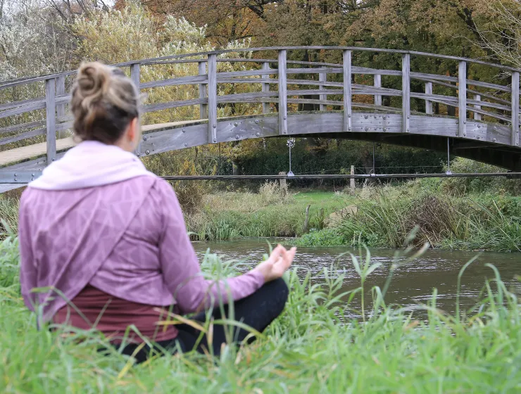 vrouw aan het mediteren in de natuur bij een brug